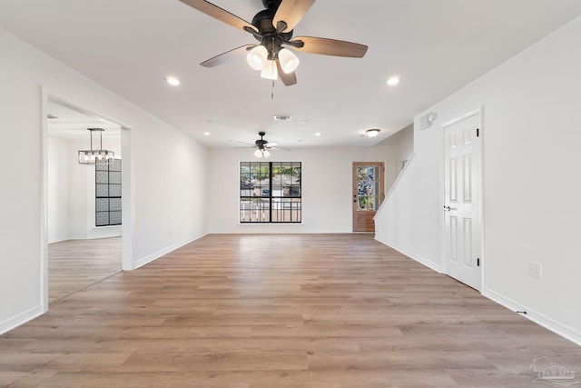 unfurnished living room with light wood-type flooring, visible vents, ceiling fan with notable chandelier, recessed lighting, and baseboards