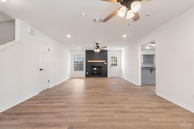 unfurnished living room with visible vents, recessed lighting, a large fireplace, light wood finished floors, and baseboards