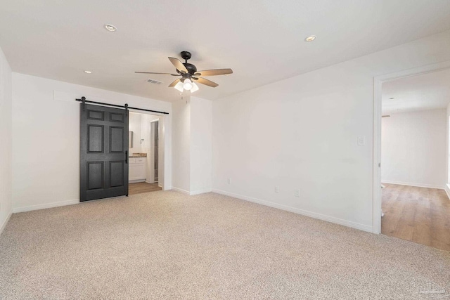 empty room featuring a barn door, a ceiling fan, baseboards, and light carpet