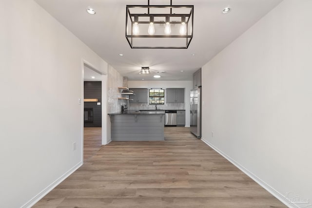 kitchen featuring dark countertops, backsplash, gray cabinets, appliances with stainless steel finishes, and light wood-style flooring