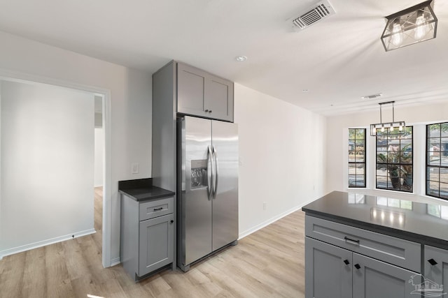 kitchen with visible vents, light wood finished floors, gray cabinets, stainless steel refrigerator with ice dispenser, and dark countertops