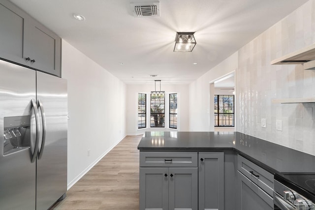 kitchen with a peninsula, dark countertops, gray cabinets, and stainless steel appliances