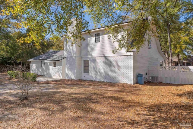 back of property featuring brick siding, central AC unit, a chimney, and fence