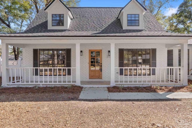 view of front of home featuring covered porch, brick siding, and roof with shingles