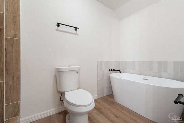 bathroom featuring a soaking tub, toilet, baseboards, and wood finished floors