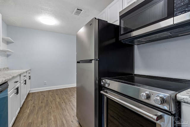 kitchen with light stone counters, light hardwood / wood-style floors, white cabinets, and appliances with stainless steel finishes