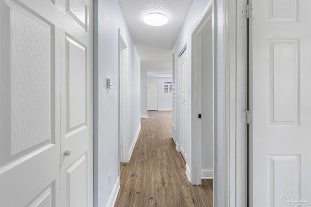 hallway with light hardwood / wood-style floors and a textured ceiling