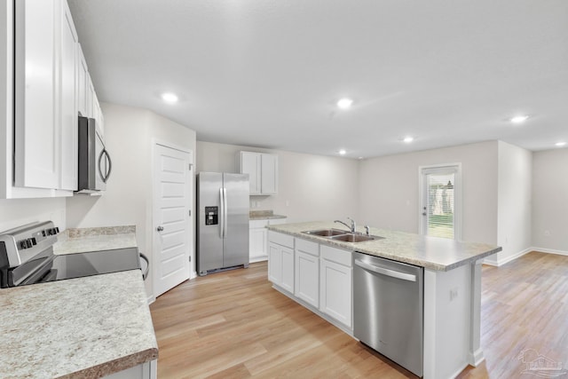 kitchen featuring appliances with stainless steel finishes, white cabinetry, light wood-type flooring, a center island with sink, and sink