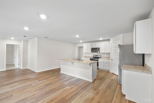 kitchen featuring appliances with stainless steel finishes, white cabinetry, light wood-type flooring, a center island with sink, and sink