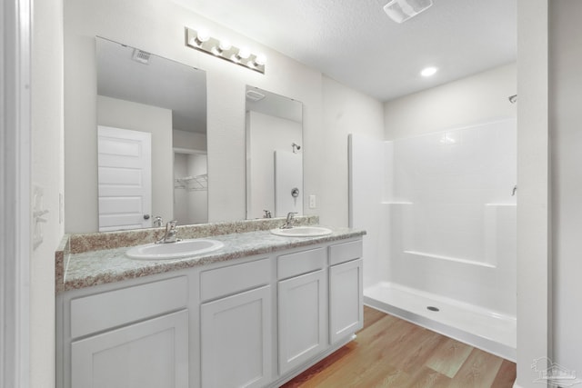 bathroom with hardwood / wood-style floors, a textured ceiling, walk in shower, and vanity