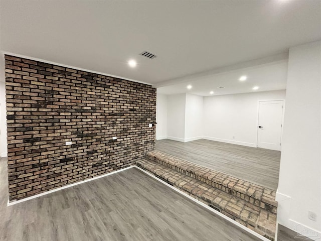 basement with brick wall and hardwood / wood-style flooring