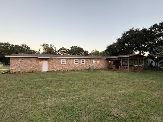 back house at dusk with a lawn and central AC