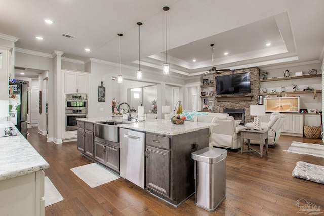 kitchen featuring a sink, appliances with stainless steel finishes, a stone fireplace, ceiling fan, and crown molding