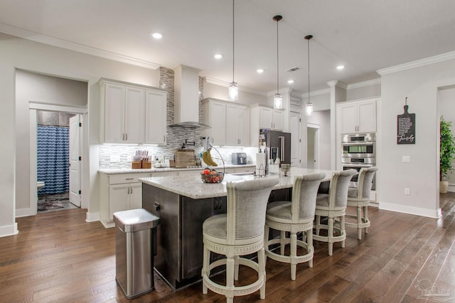 kitchen with wall chimney range hood, stainless steel appliances, decorative backsplash, dark wood-style flooring, and a spacious island