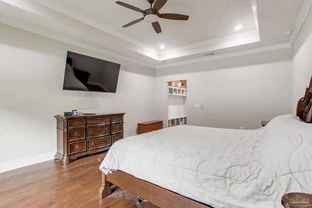 bedroom with wood finished floors, a tray ceiling, ornamental molding, baseboards, and recessed lighting