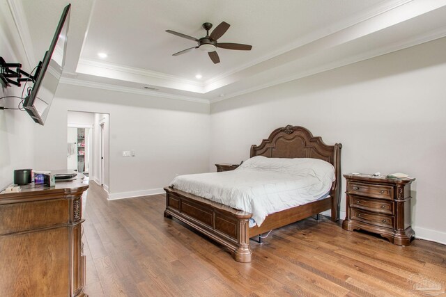 bedroom featuring a raised ceiling, crown molding, wood finished floors, baseboards, and recessed lighting