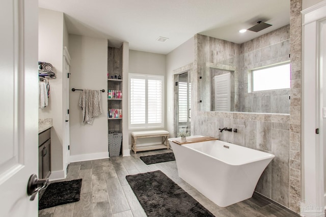 full bathroom with a tile shower, tile walls, a freestanding bath, vanity, and wood finished floors