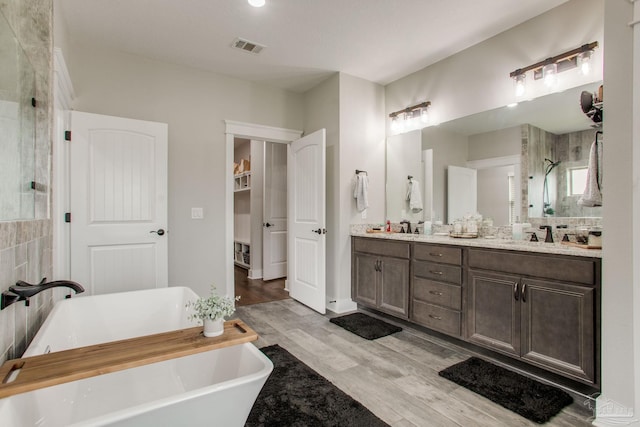 bathroom with wood finished floors, a freestanding bath, double vanity, and an enclosed shower