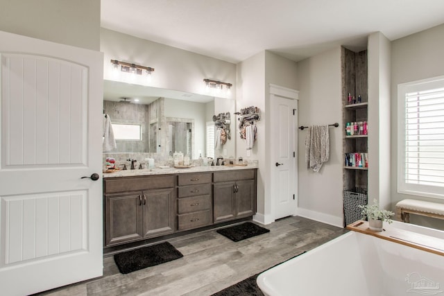 full bathroom with wood finished floors, plenty of natural light, double vanity, and baseboards