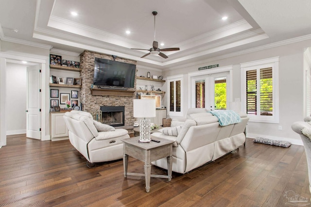 living area with a tray ceiling, a ceiling fan, dark wood-style flooring, ornamental molding, and a fireplace
