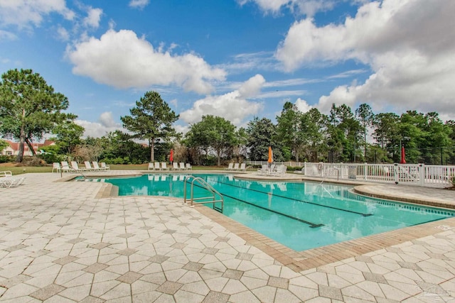 community pool with a patio area, fence, and view of wooded area