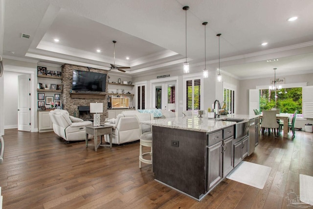 kitchen with a tray ceiling, a sink, dark wood-style floors, a breakfast bar, and a stone fireplace