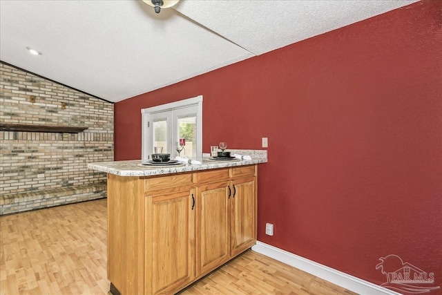 kitchen featuring brick wall, light countertops, a peninsula, lofted ceiling, and light wood-style floors