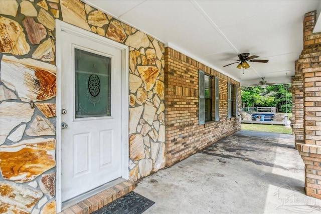 property entrance featuring a porch, a ceiling fan, and brick siding