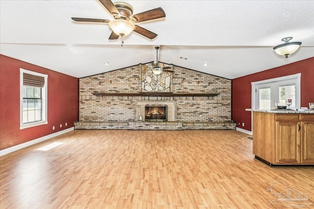 unfurnished living room featuring a brick fireplace, lofted ceiling, brick wall, light wood-style floors, and a ceiling fan