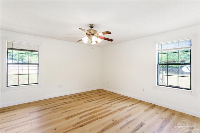 unfurnished room with light wood-type flooring, a ceiling fan, baseboards, and a healthy amount of sunlight