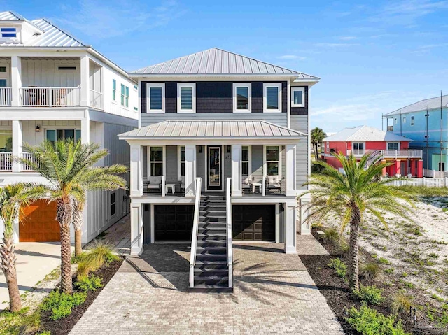 raised beach house featuring a standing seam roof, stairs, metal roof, decorative driveway, and a garage