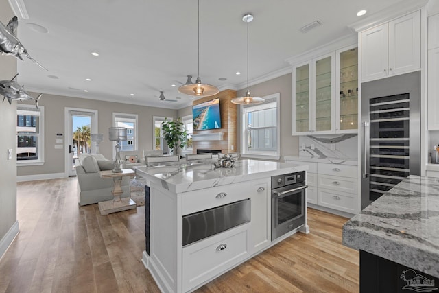 kitchen with light wood finished floors, white cabinets, wine cooler, and stainless steel oven