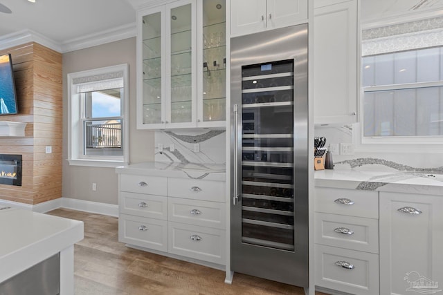 kitchen with crown molding, wine cooler, white cabinets, light wood-style flooring, and glass insert cabinets