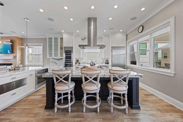 kitchen featuring an island with sink, island range hood, white cabinets, and stainless steel appliances