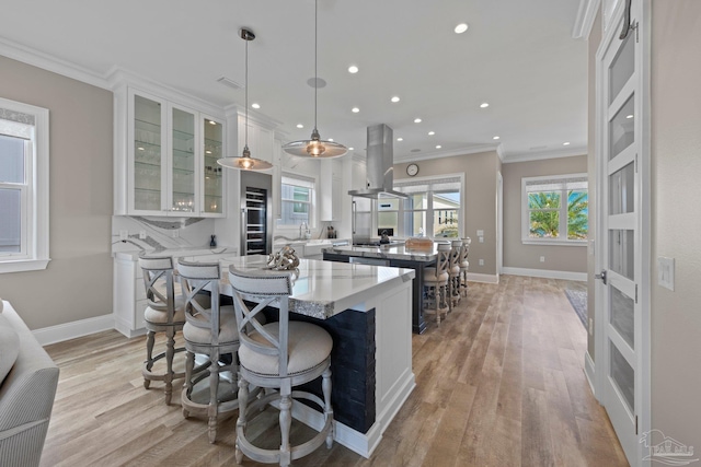 kitchen with a large island, light wood-style flooring, island exhaust hood, and ornamental molding
