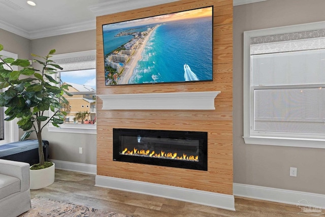 interior details with crown molding, baseboards, visible vents, a glass covered fireplace, and wood finished floors