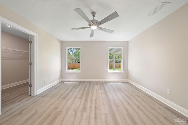 unfurnished bedroom featuring light wood-type flooring, a textured ceiling, a spacious closet, a closet, and ceiling fan