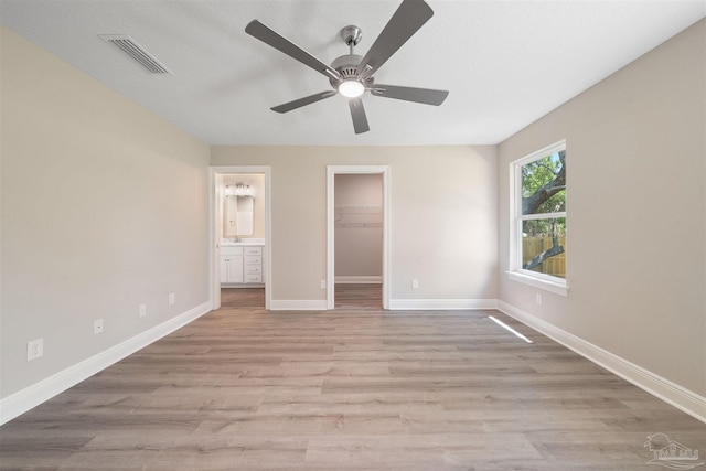 unfurnished bedroom featuring a spacious closet, light hardwood / wood-style floors, ceiling fan, and connected bathroom