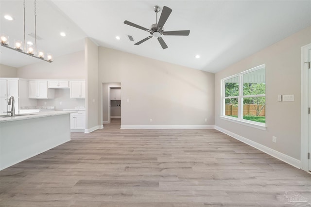 unfurnished living room with sink, high vaulted ceiling, light hardwood / wood-style floors, and ceiling fan with notable chandelier