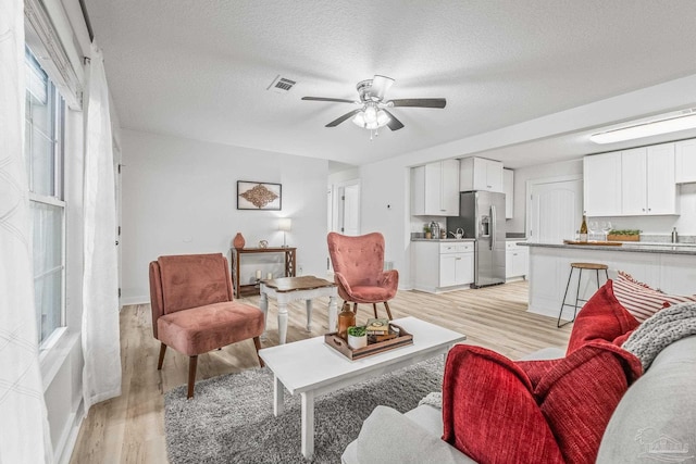 living room featuring ceiling fan, light hardwood / wood-style flooring, and a textured ceiling