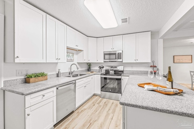 kitchen featuring appliances with stainless steel finishes, light stone counters, sink, light hardwood / wood-style flooring, and white cabinets