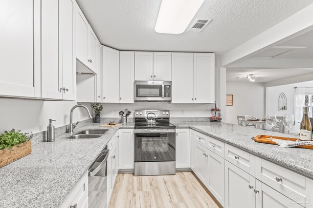 kitchen featuring white cabinets, sink, light wood-type flooring, a textured ceiling, and appliances with stainless steel finishes