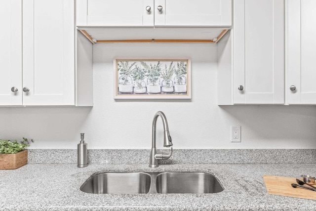 kitchen featuring white cabinets, light stone counters, and sink