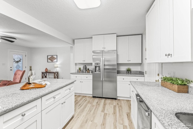 kitchen with white cabinets, ceiling fan, appliances with stainless steel finishes, light hardwood / wood-style floors, and light stone counters