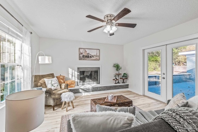 living room featuring ceiling fan, french doors, a textured ceiling, and light wood-type flooring