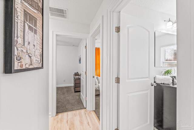 hallway with light hardwood / wood-style floors and a textured ceiling