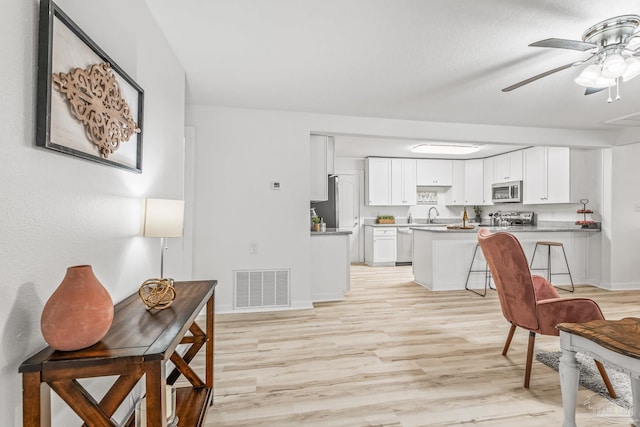 kitchen featuring light wood-type flooring, stainless steel appliances, ceiling fan, sink, and white cabinetry