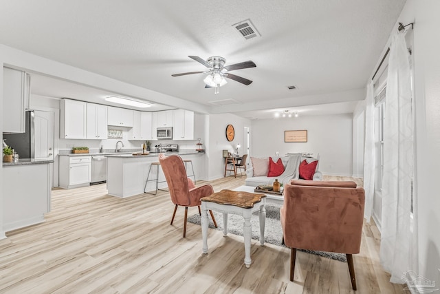 living room with ceiling fan, sink, a textured ceiling, and light wood-type flooring