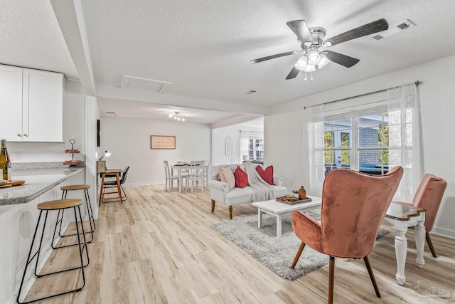 living room featuring a textured ceiling, light wood-type flooring, and ceiling fan