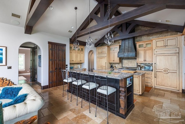 3063 Bay St, Gulf Breeze, FL 32563 - kitchen with stone tile flooring, a large island with sink, arched walkways, beamed ceiling, and premium range hood